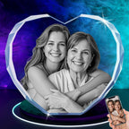 A personalized 3D crystal photo frame in the shape of a heart, featuring an image of two smiling women embracing. The crystal frame has a transparent color with a heart shape, displayed on a blue and black background.
